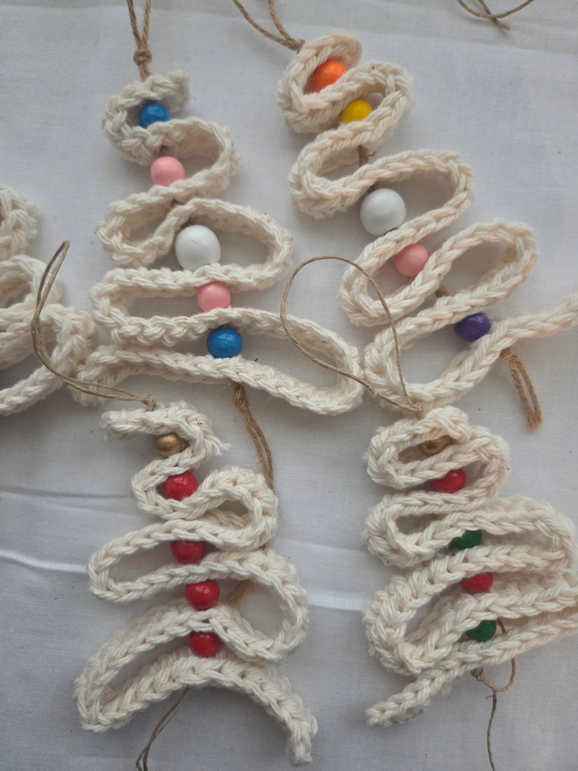Handmade crochet Christmas tree ornaments with colorful beads on white fabric