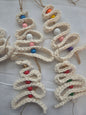 Handmade crochet Christmas tree ornaments with colorful beads on white fabric