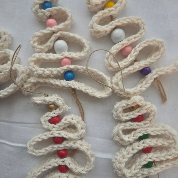 Handmade crochet Christmas tree ornaments with colorful beads on white fabric