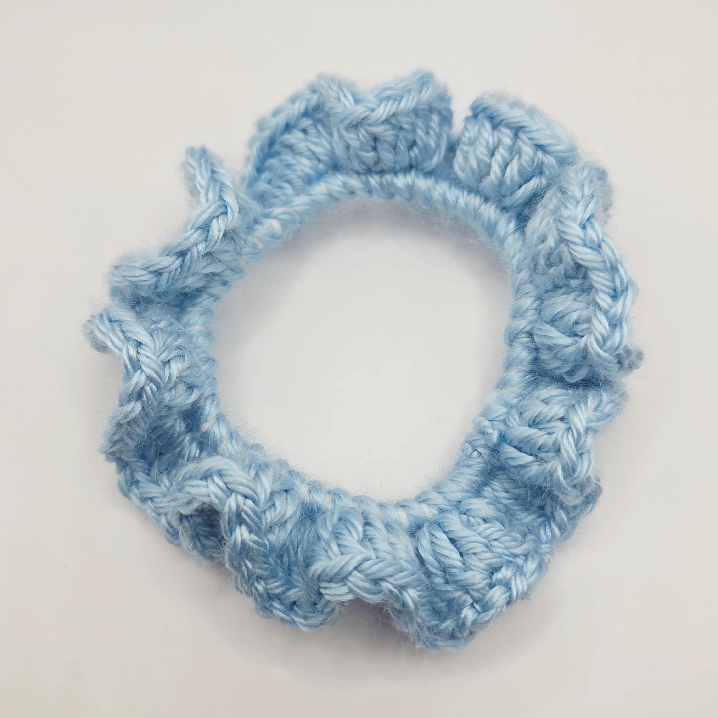 Handmade light blue crochet scrunchie on white background, cozy hair accessory