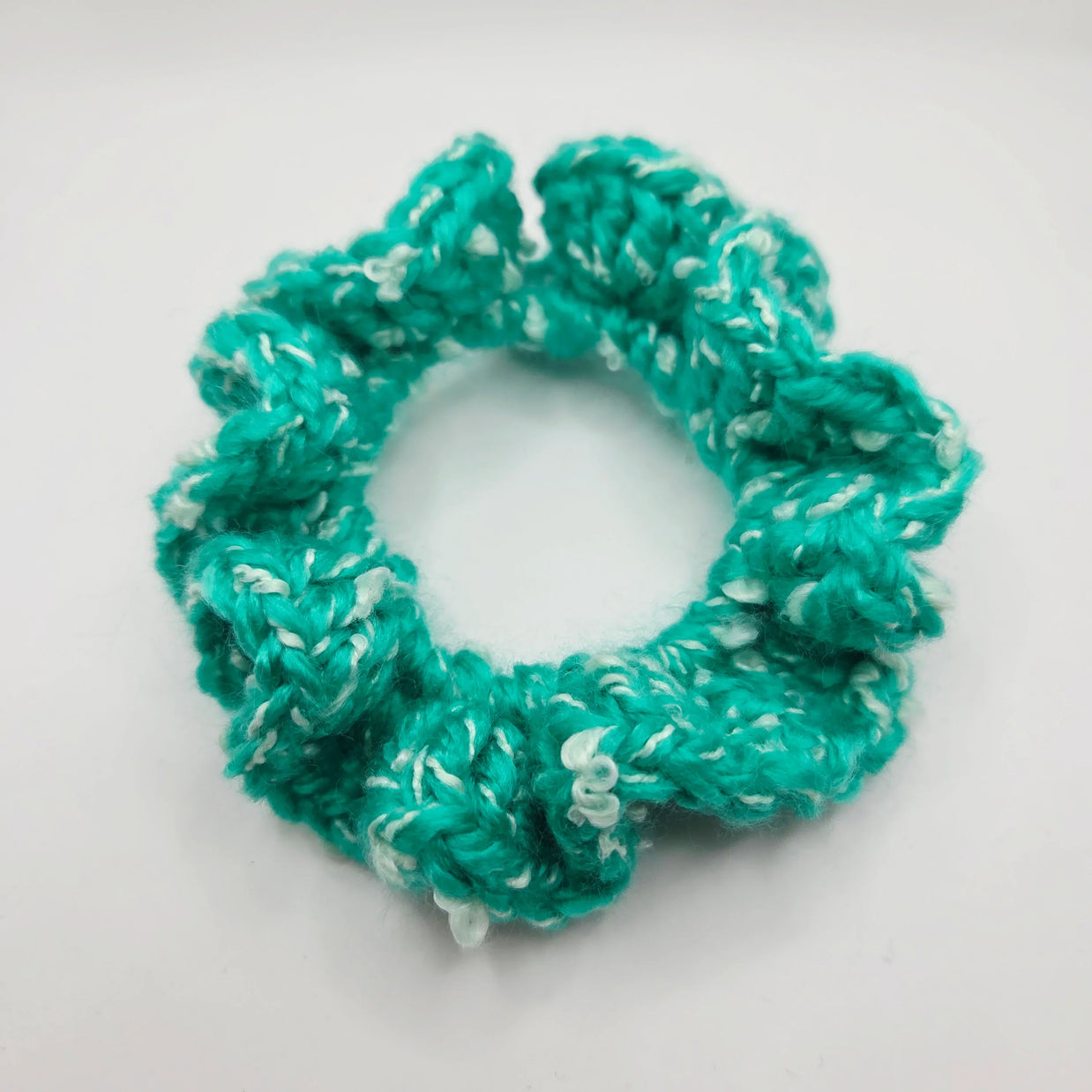 Handmade turquoise crochet scrunchie with white accents on white background