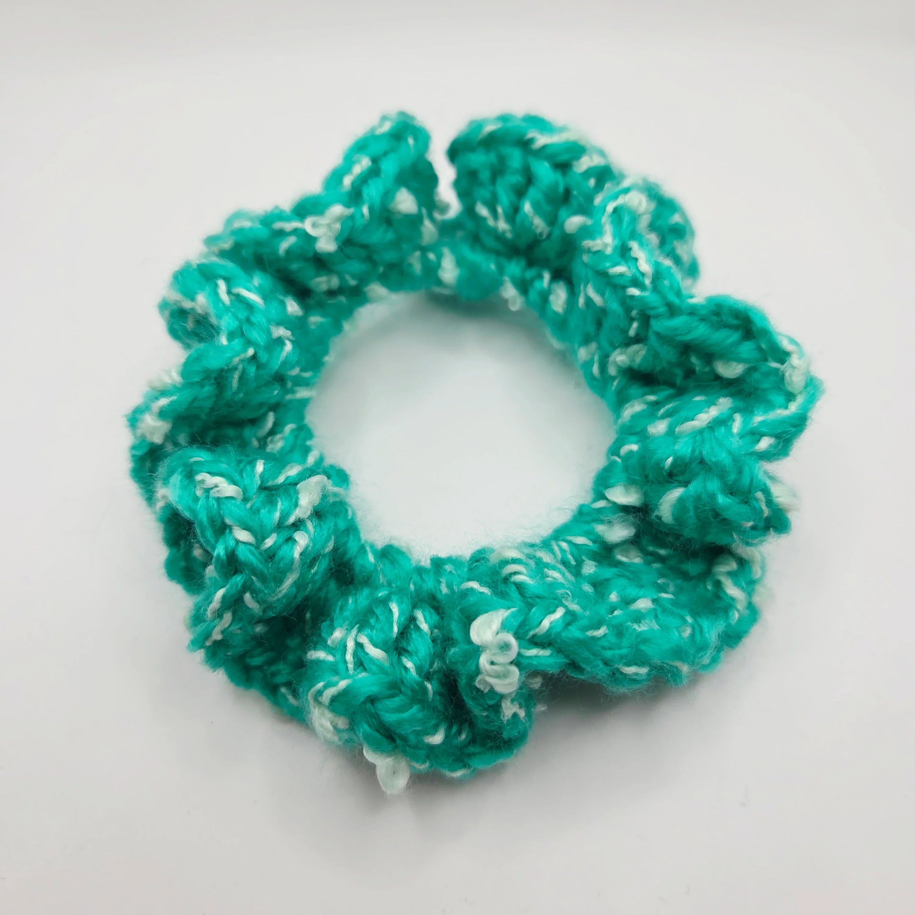 Handmade turquoise crochet scrunchie with white accents on white background