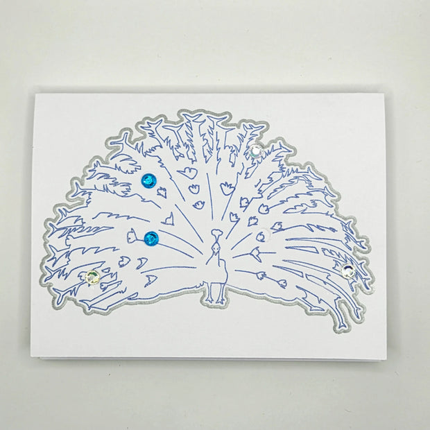Handmade card with blue peacock outline, heart details, and sparkling sequin accents
