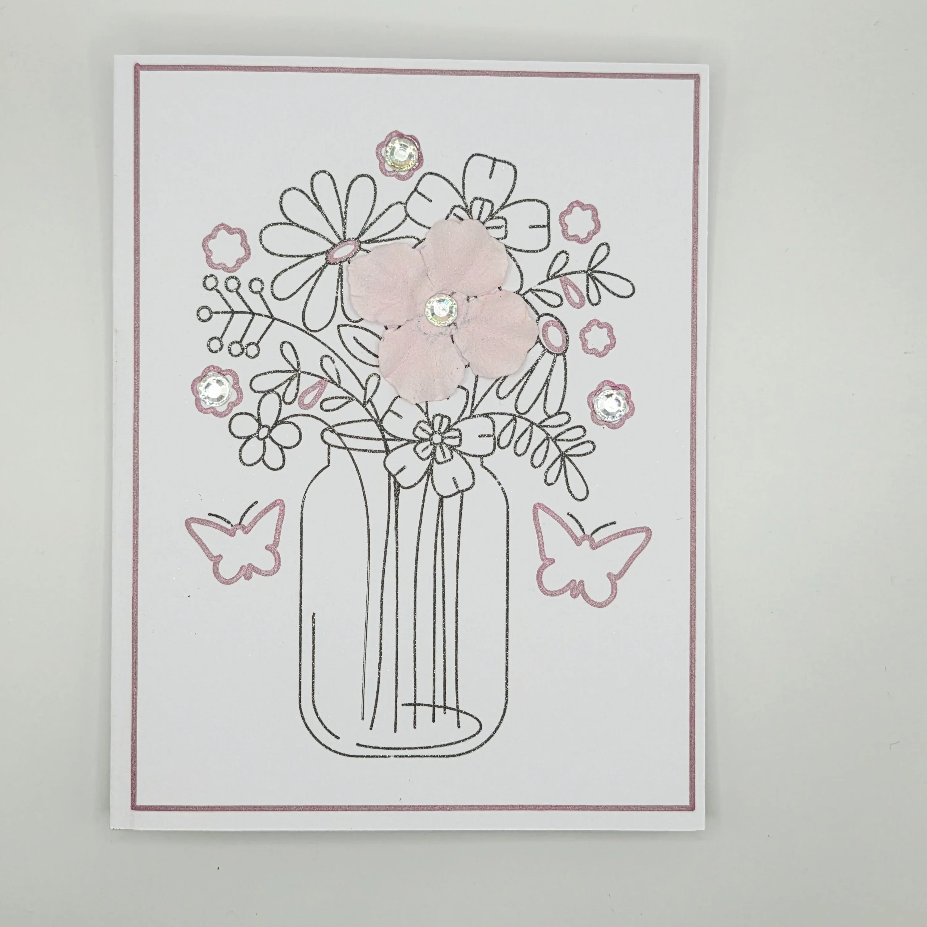 Handmade floral greeting card with pink fabric flowers, butterflies, and glitter accents