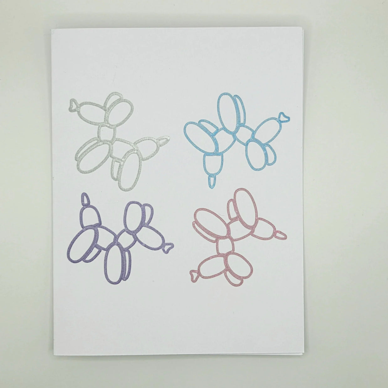 Four glittery balloon animal designs in silver, blue, purple, and pink on white paper