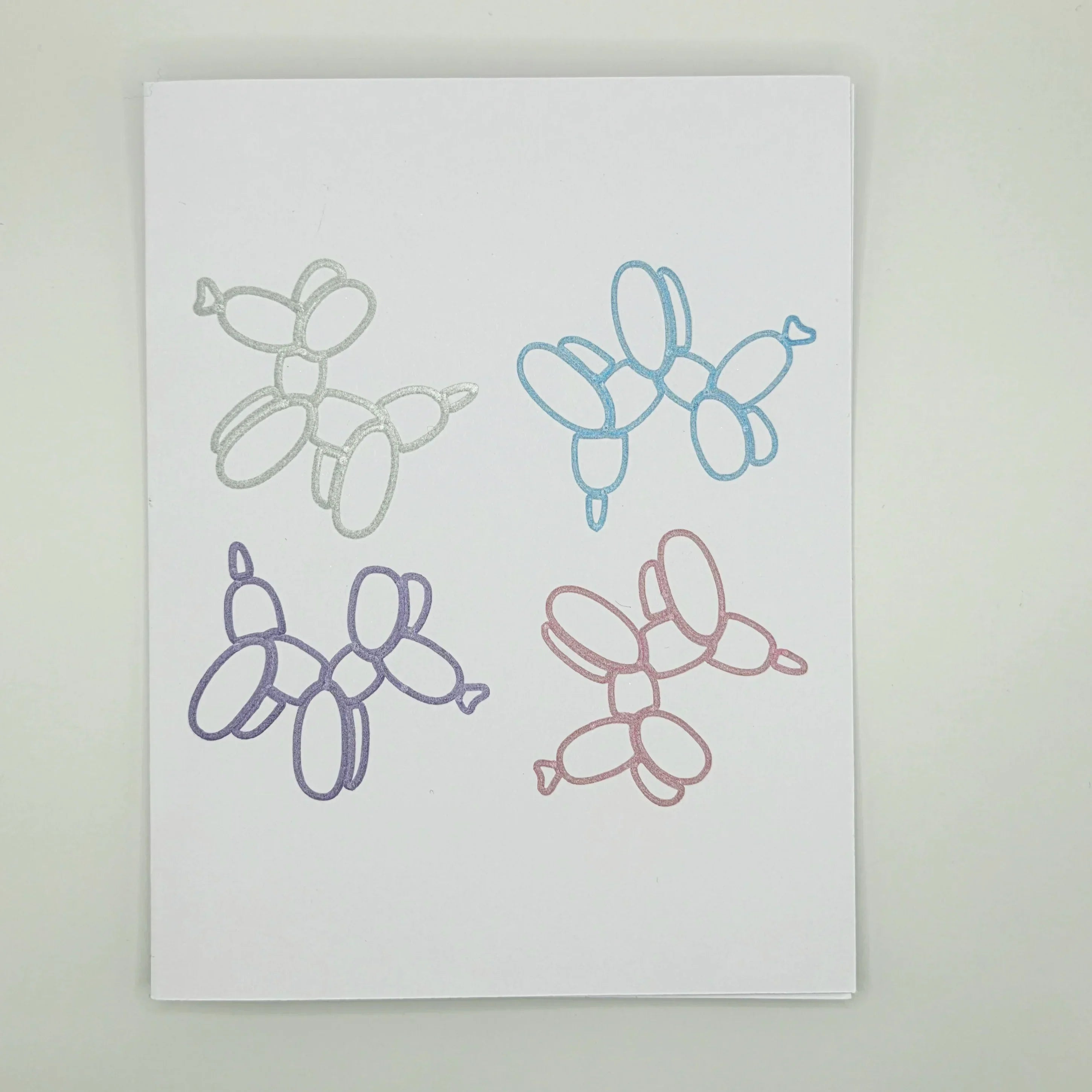 Four glittery balloon animal designs in silver, blue, purple, and pink on white paper