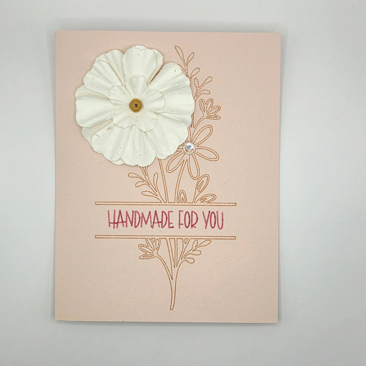 Handmade card with white paper flower, floral design, and 'Handmade for You' text on pink background.
