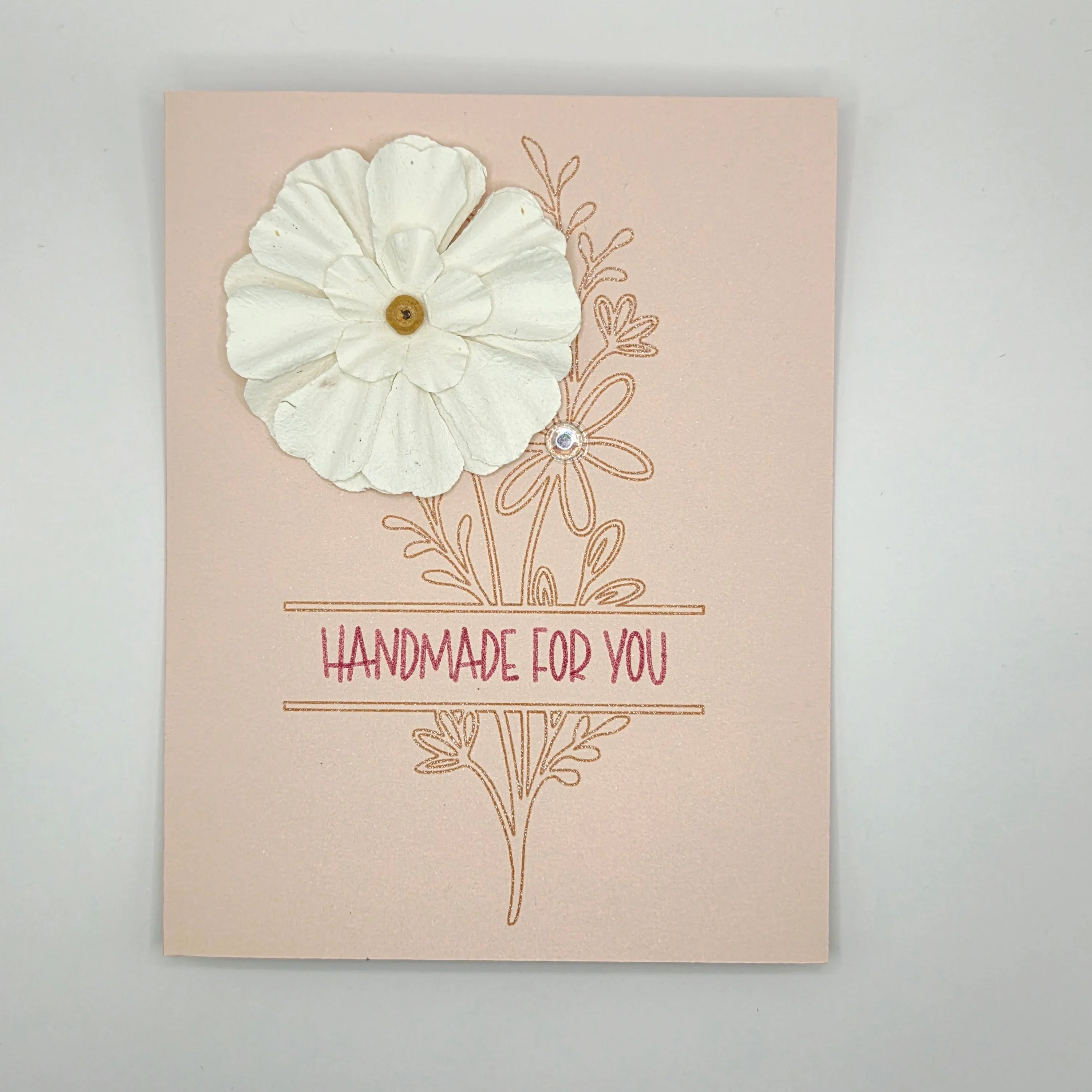 Handmade card with white paper flower, floral design, and 'Handmade for You' text on pink background.
