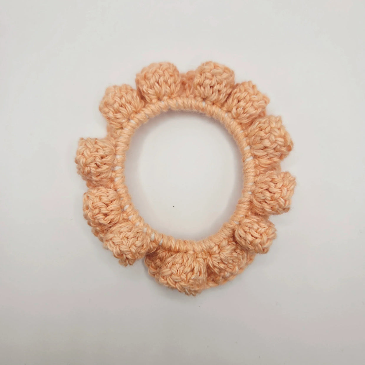 Handmade peach crochet scrunchie with textured edges on white background
