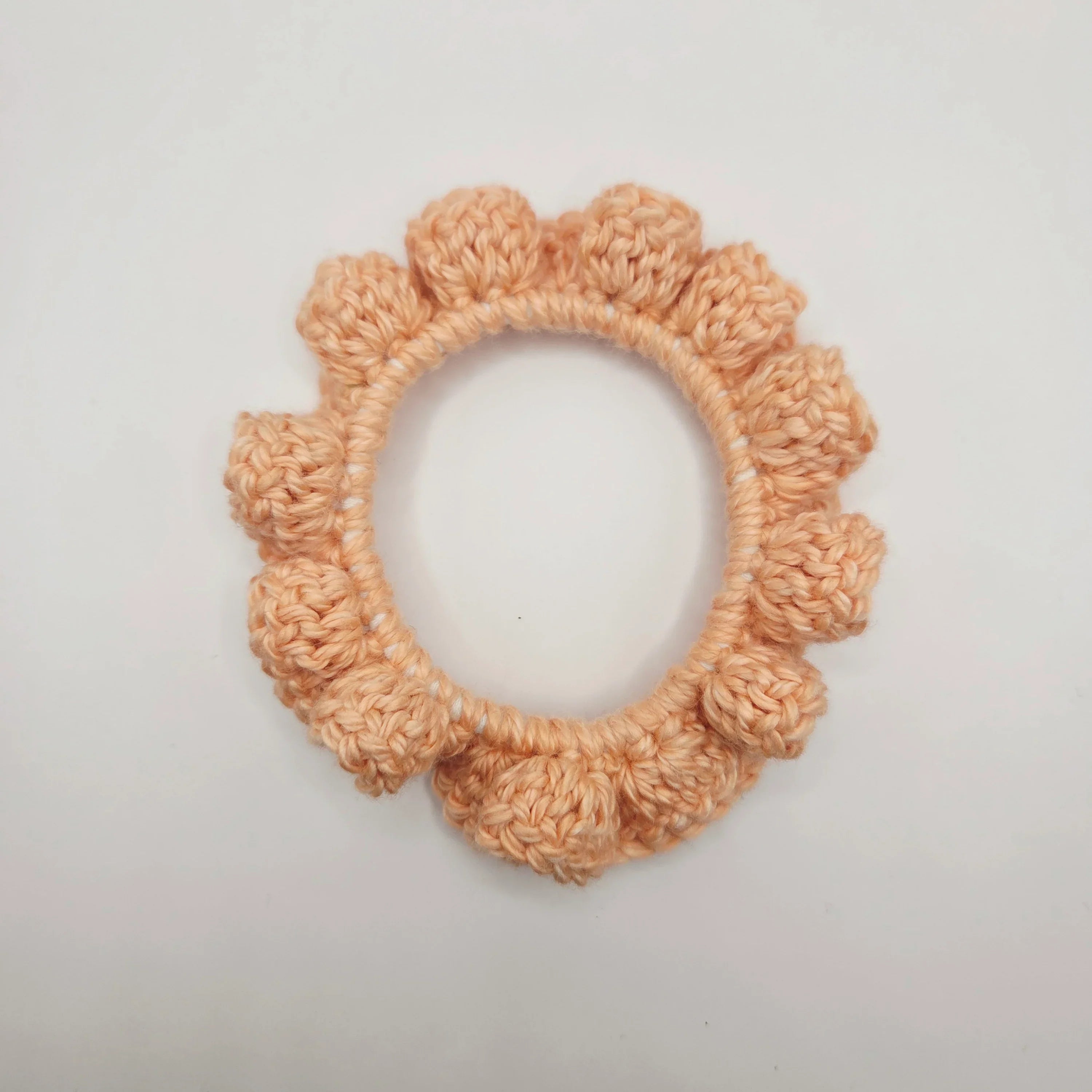 Handmade peach crochet scrunchie with textured edges on white background