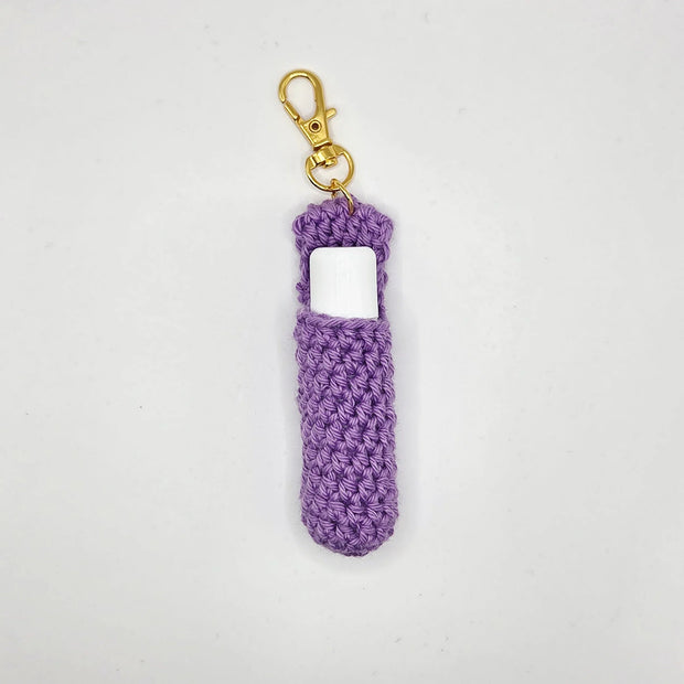 Handmade crochet lip balm holder keychain in purple with gold clasp on white background