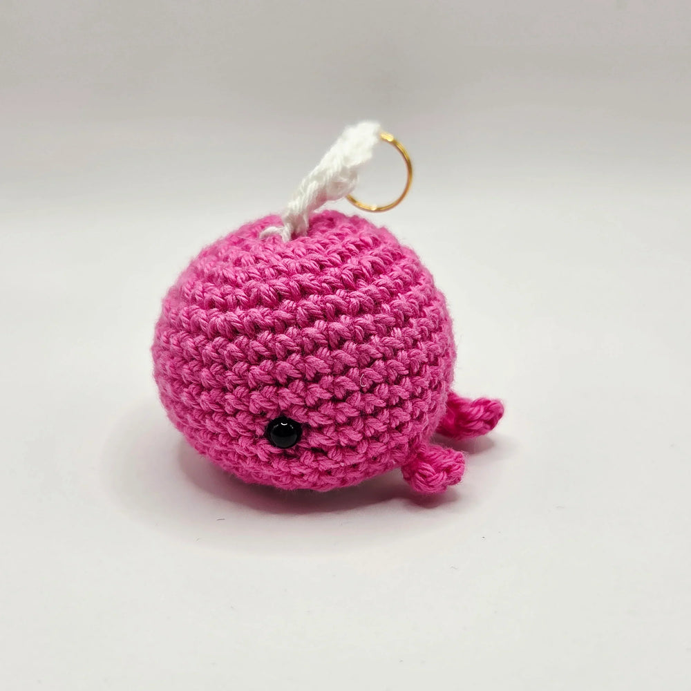 Handmade pink crochet whale keychain with black eye and gold ring, cozy amigurumi gift