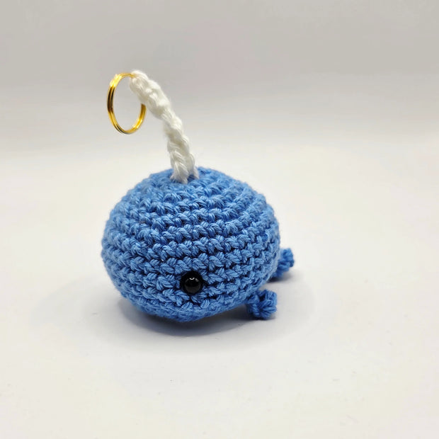 Handmade blue crochet whale keychain with gold ring on white background