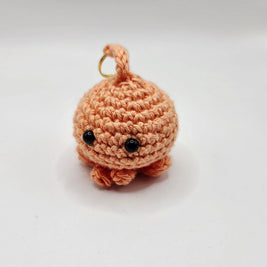 Handmade crochet octopus keychain in peach yarn with black eyes, on white background