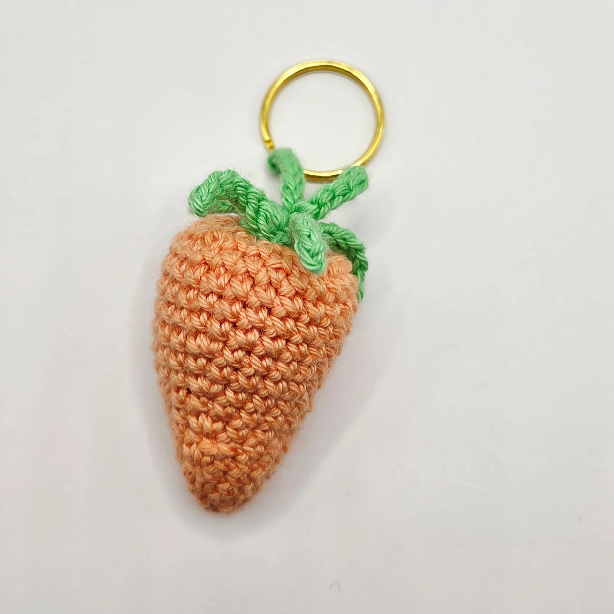 Handmade crochet carrot keychain with green leaves on a white background