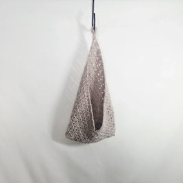 Handmade crochet bag in beige yarn hanging on a hook, minimal cozy design