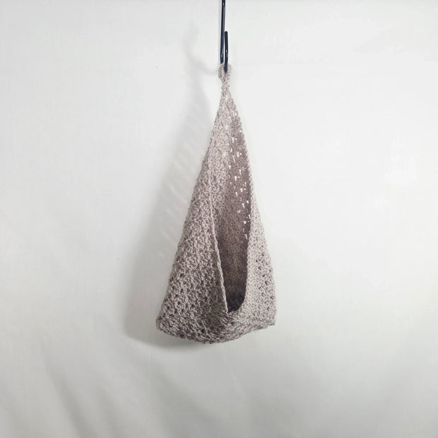 Handmade crochet bag in beige yarn hanging on a hook, minimal cozy design
