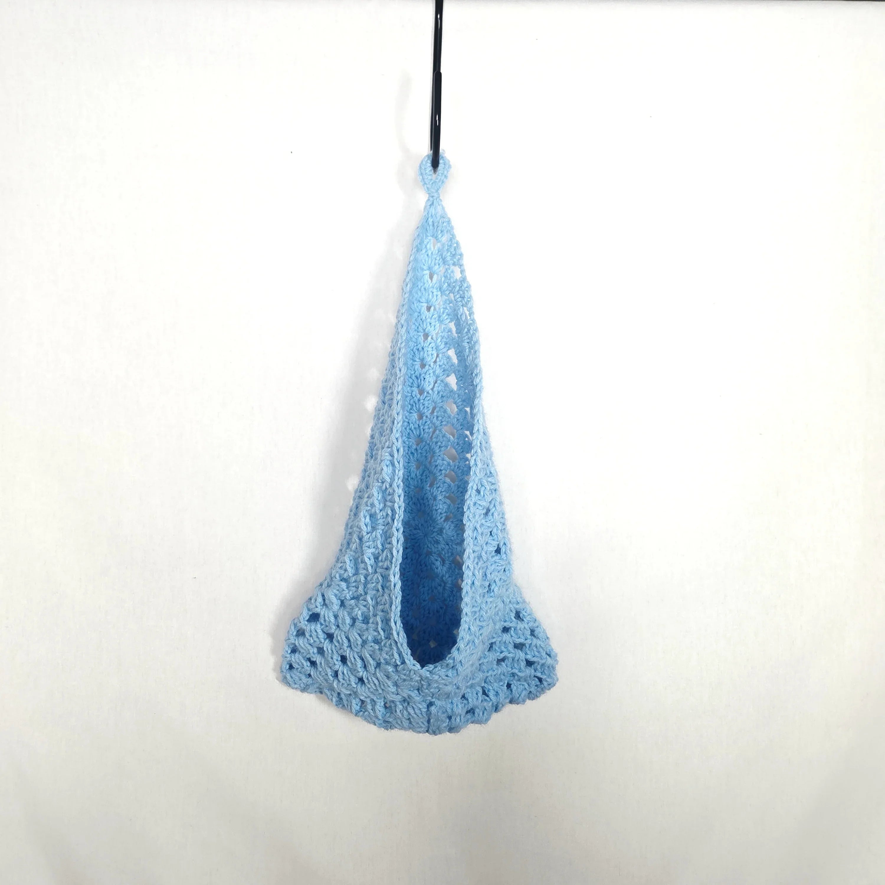 Handmade light blue crochet bag hanging on white background, cozy and creative gift
