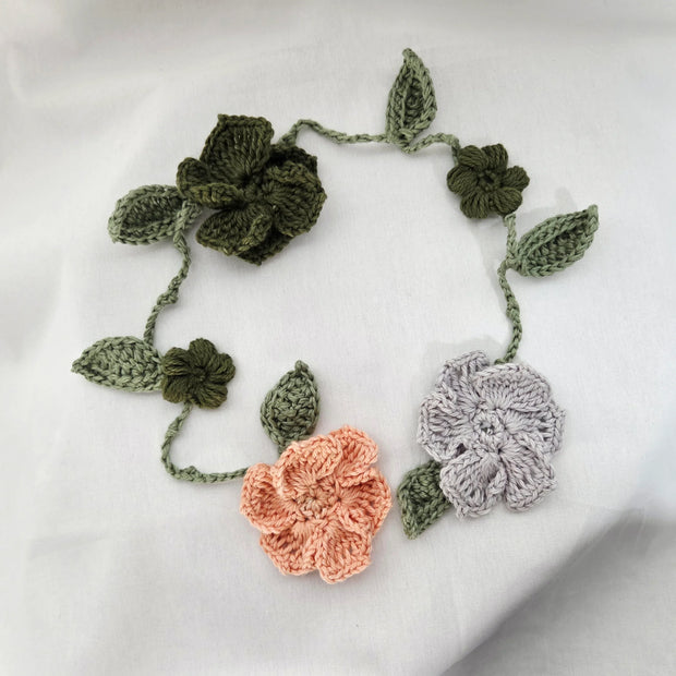 Handmade crochet flower garland with green leaves on white fabric background