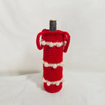 Handmade red crochet wine bottle cozy with white pom-pom trim, perfect for cozy holiday gifting.