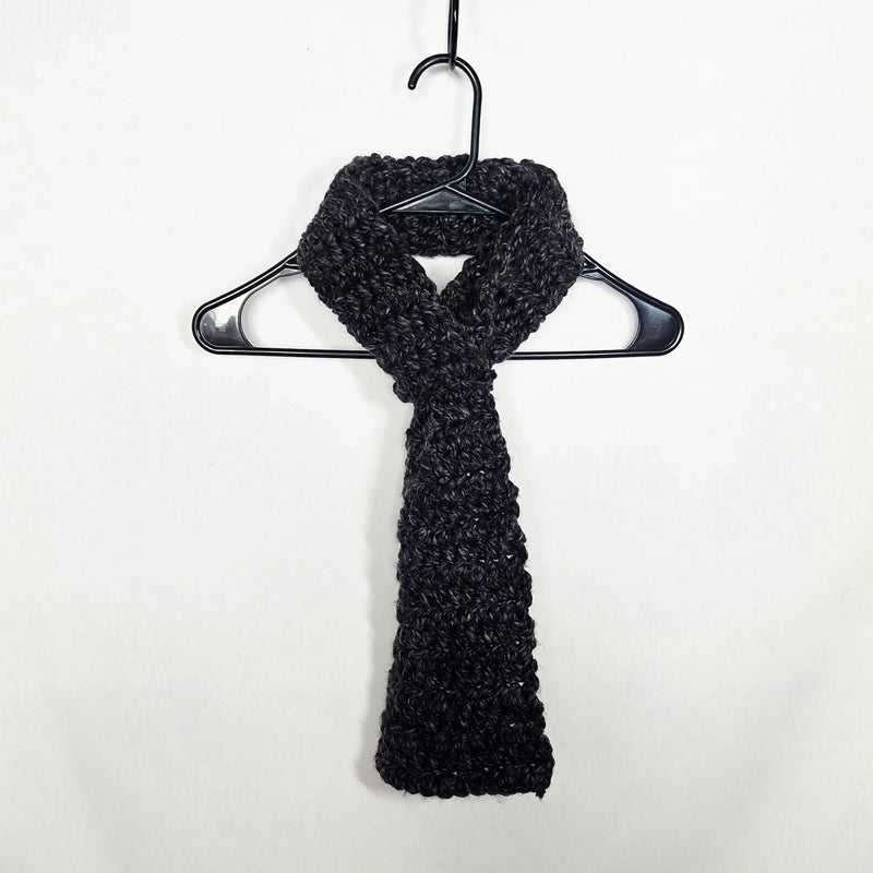 Handmade black crochet scarf draped on hanger, cozy winter accessory for warmth and style