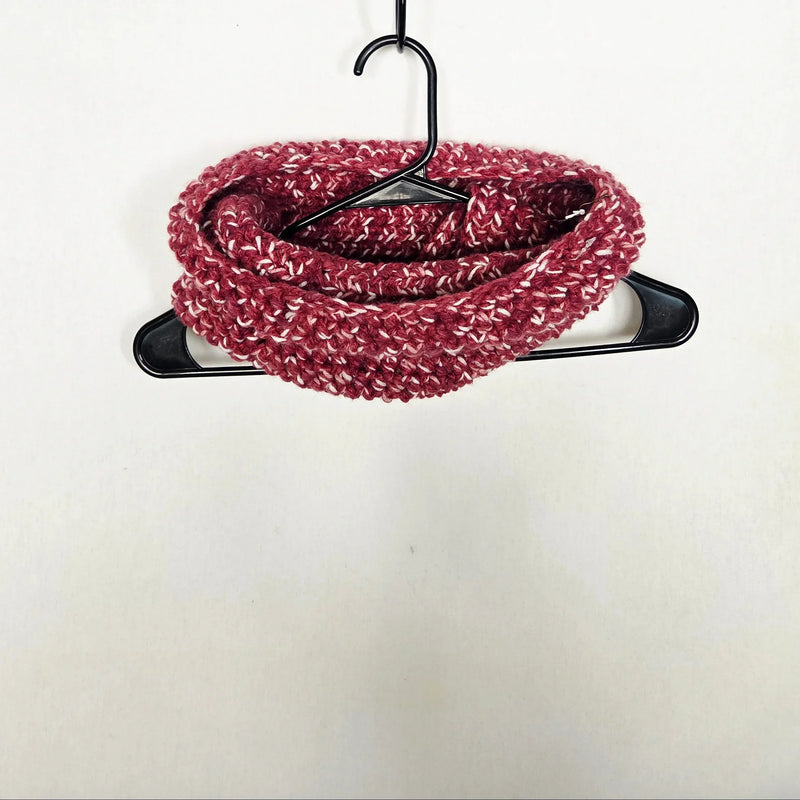 Handmade crochet infinity scarf in burgundy with white speckles, coiled on black hanger against white background