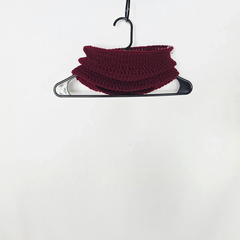 Handmade burgundy crochet scarf draped on black hanger, cozy and textured for everyday comfort