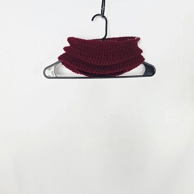 Handmade burgundy crochet cowl on hanger against white background