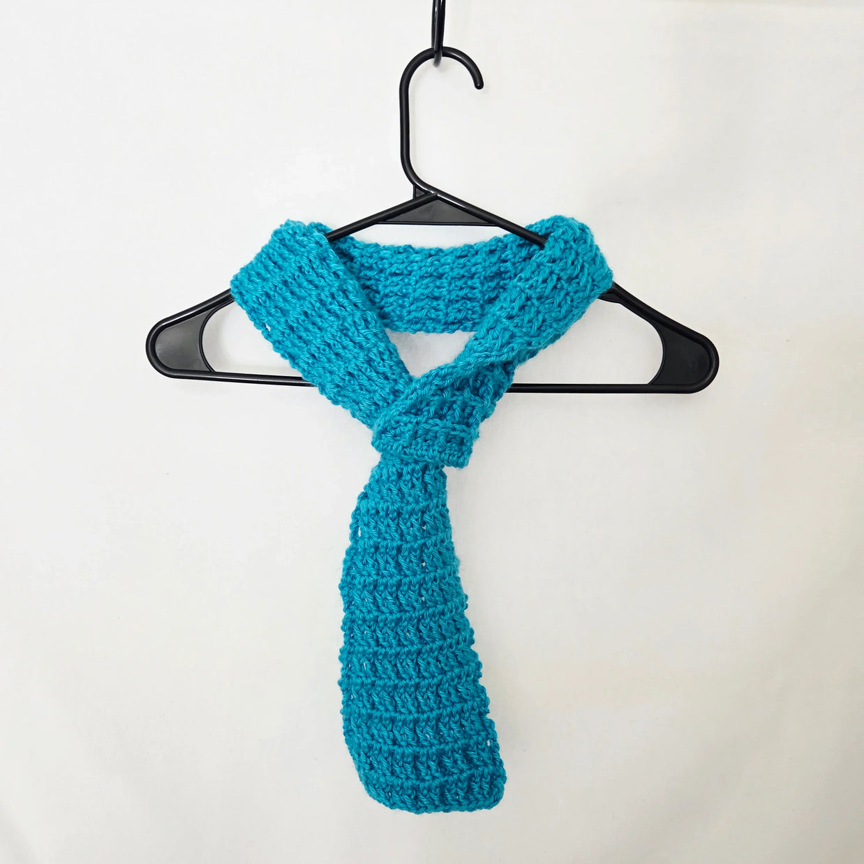 Handmade turquoise crochet scarf on black hanger against white background