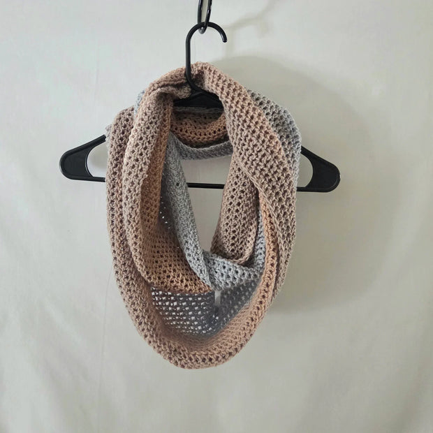 Handmade crochet infinity scarf in beige and gray, displayed on a hanger