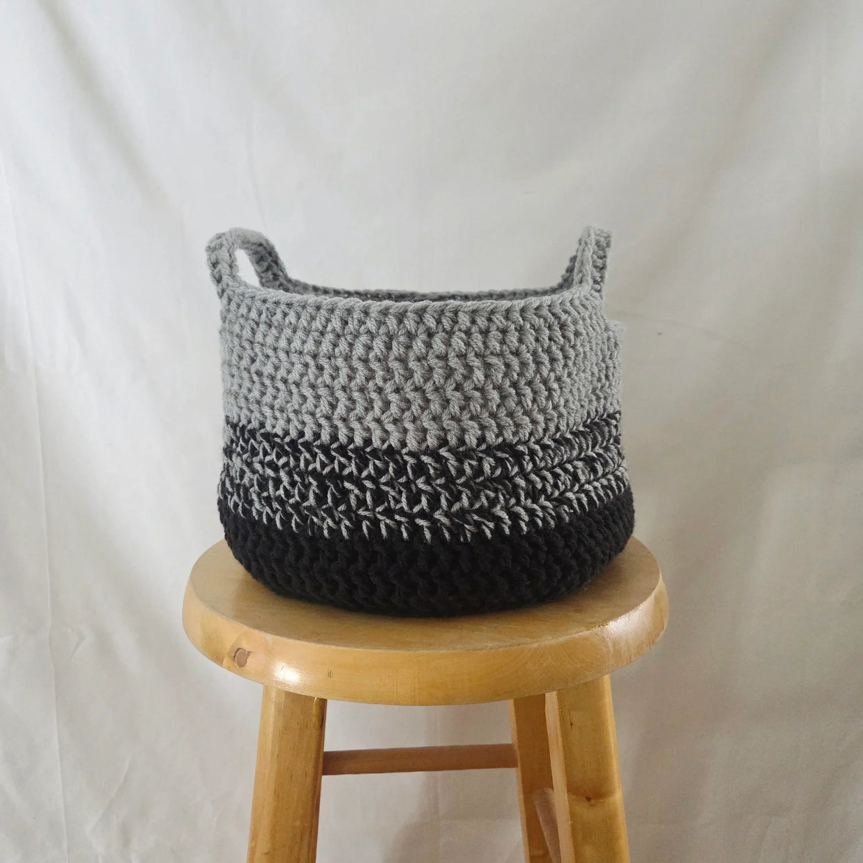 Handmade crochet basket in grey and black on a wooden stool, cozy home decor by Erika Liesel