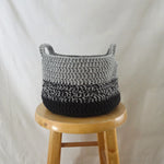 Handmade gray and black crochet basket with handles, cozy home decor on wooden stool