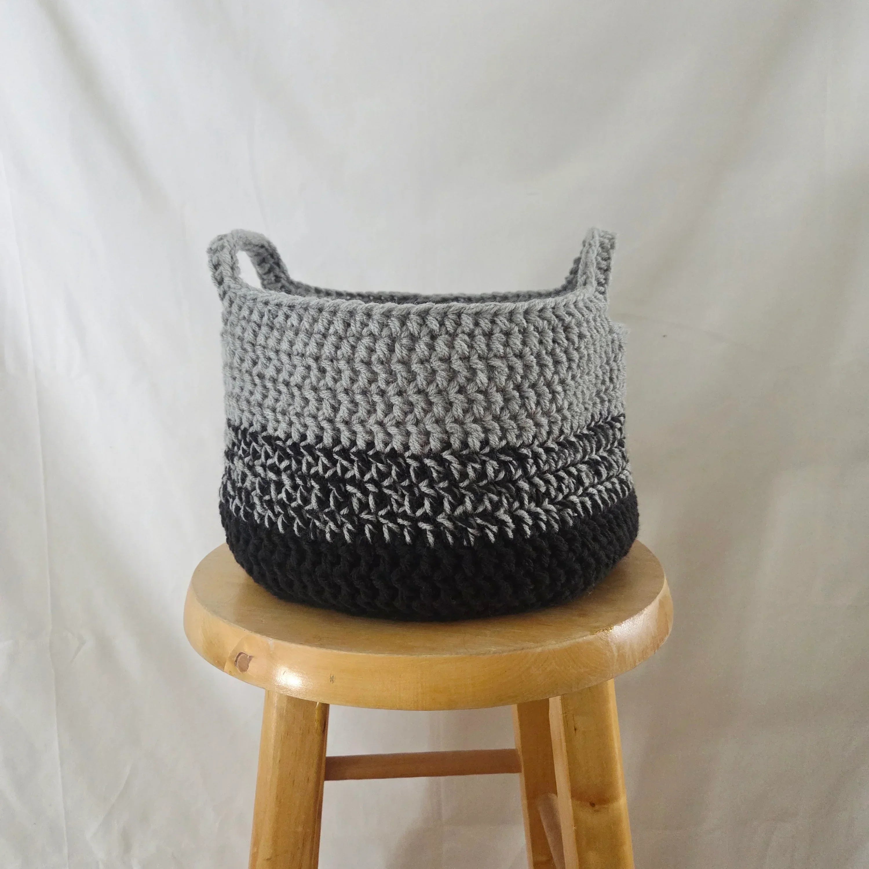 Handmade crochet basket in grey and black on a wooden stool, cozy home decor by Erika Liesel