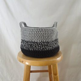 Handmade crochet basket in grey and black on a wooden stool, cozy home decor by Erika Liesel