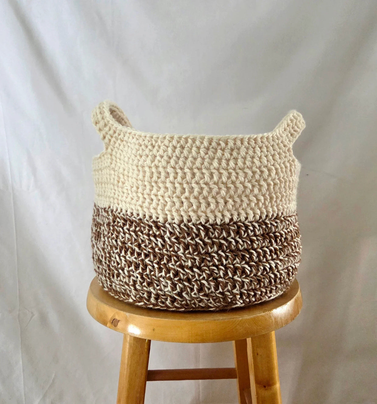 Handmade crochet storage basket in cream and brown on a wooden stool, cozy home decor