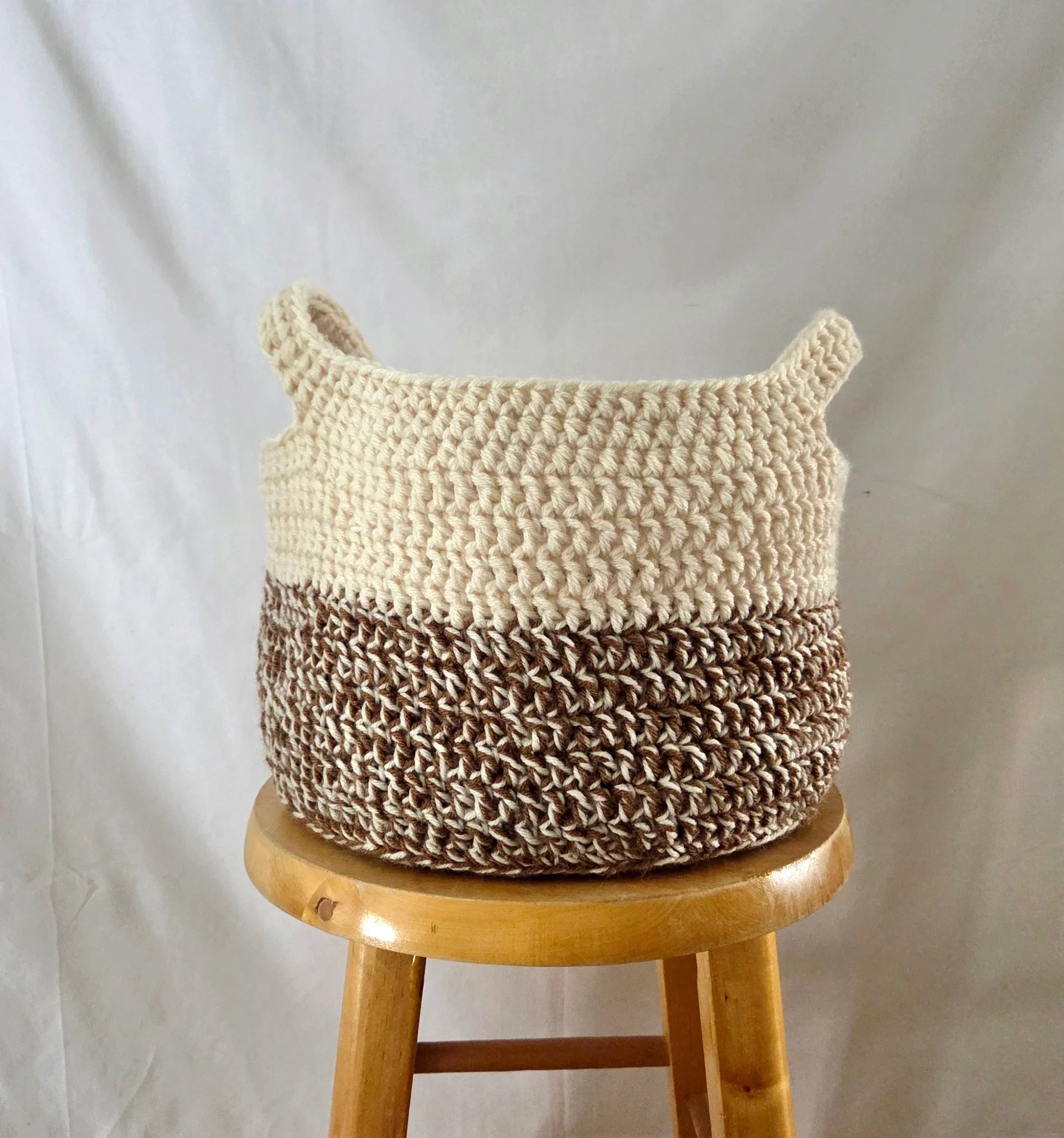 Handmade crochet storage basket in cream and brown on a wooden stool, cozy home decor