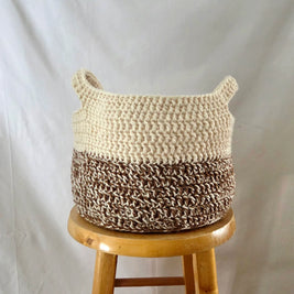 Handmade crochet storage basket in cream and brown on a wooden stool, cozy home decor
