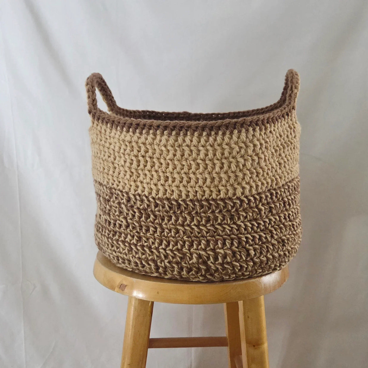 Handmade brown crochet basket on wooden stool, cozy decor by Erika Liesel