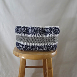 Handmade crochet storage basket with navy, white, and gray stripes on wooden stool