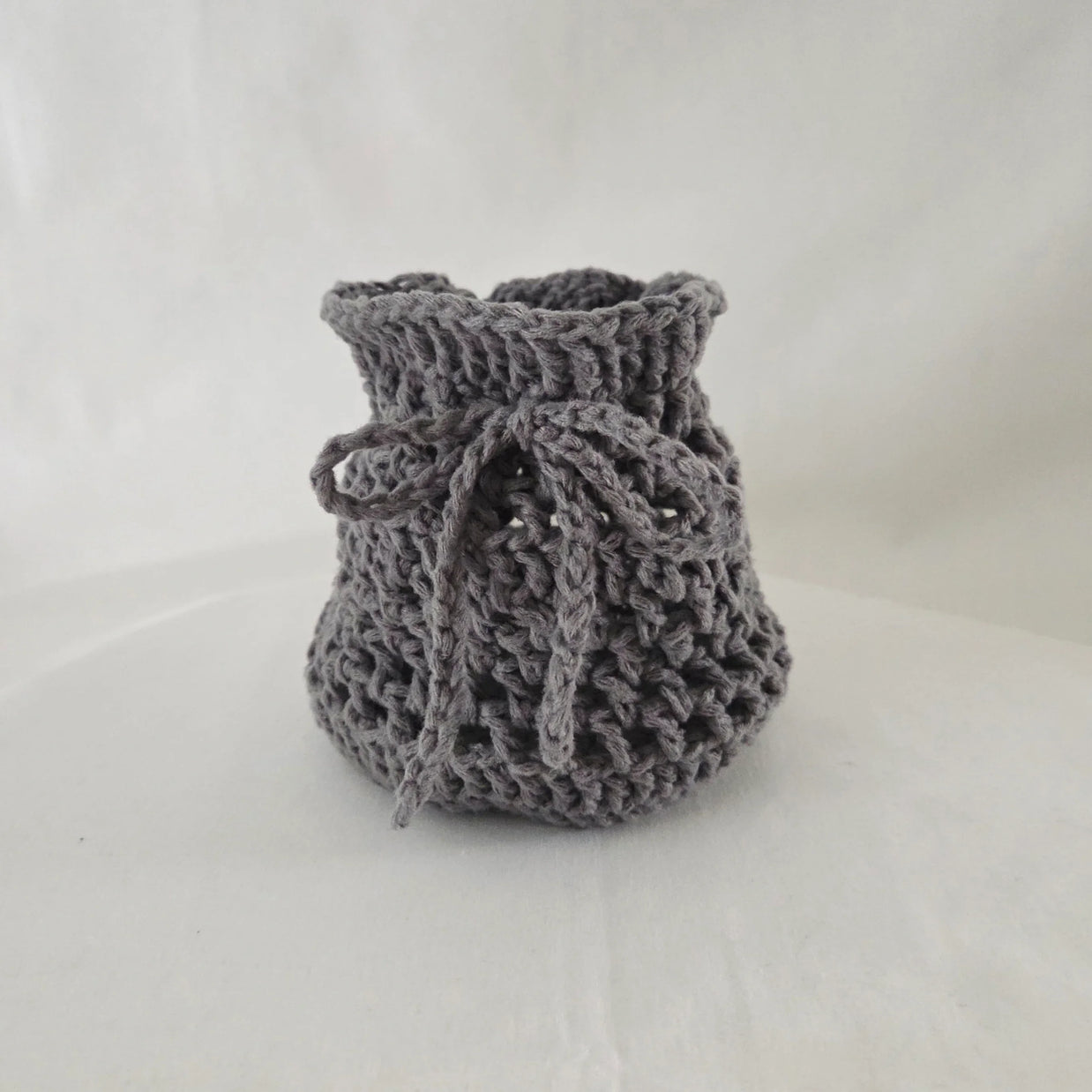 Handmade gray crochet drawstring pouch on a neutral background