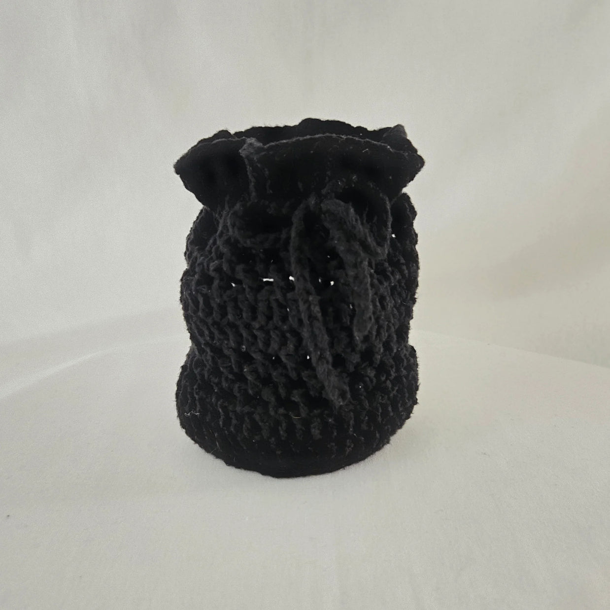 Handmade black crochet drawstring pouch on white background, cozy gift by Erika Liesel