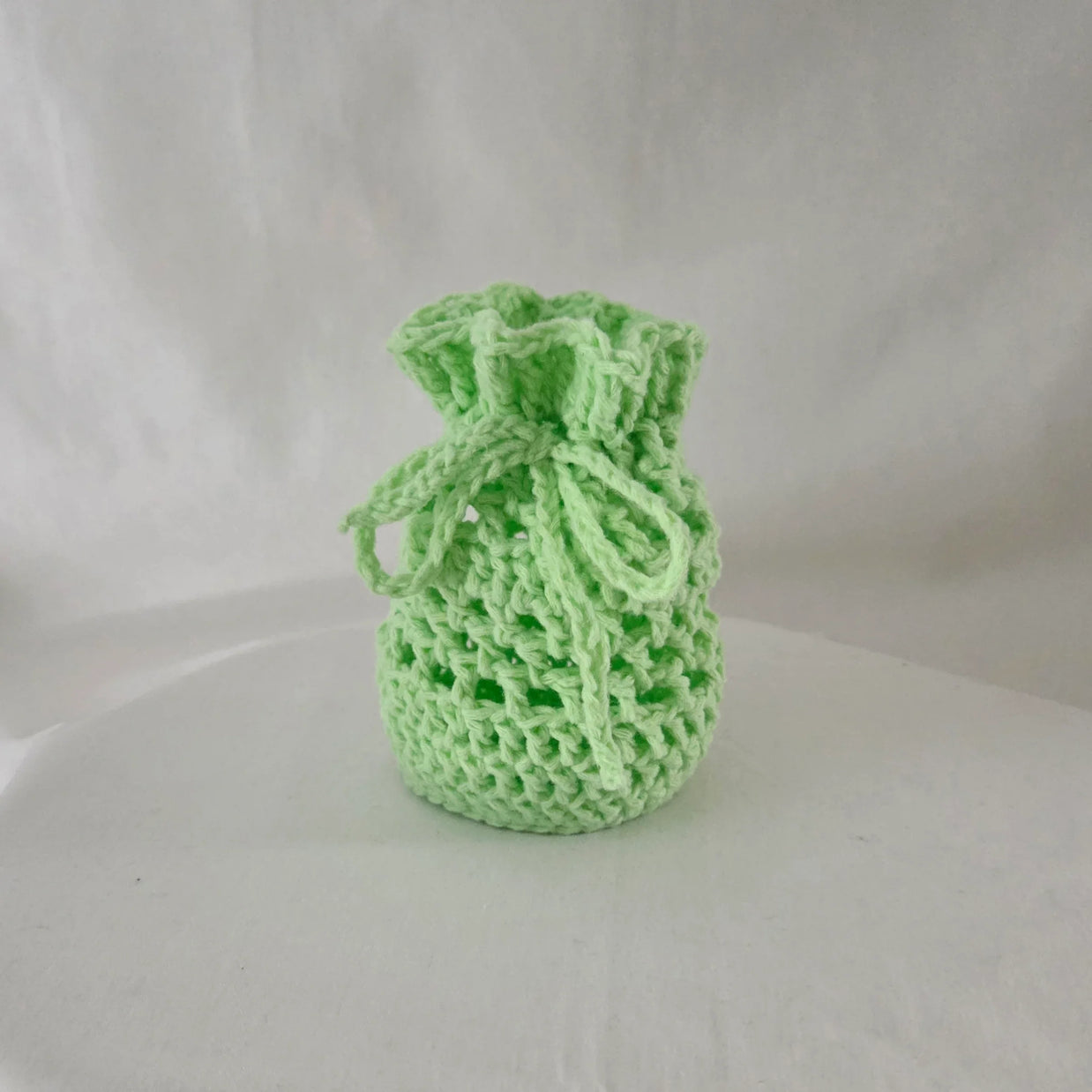 Handmade light green crochet gift bag on a white background, cozy and creative design