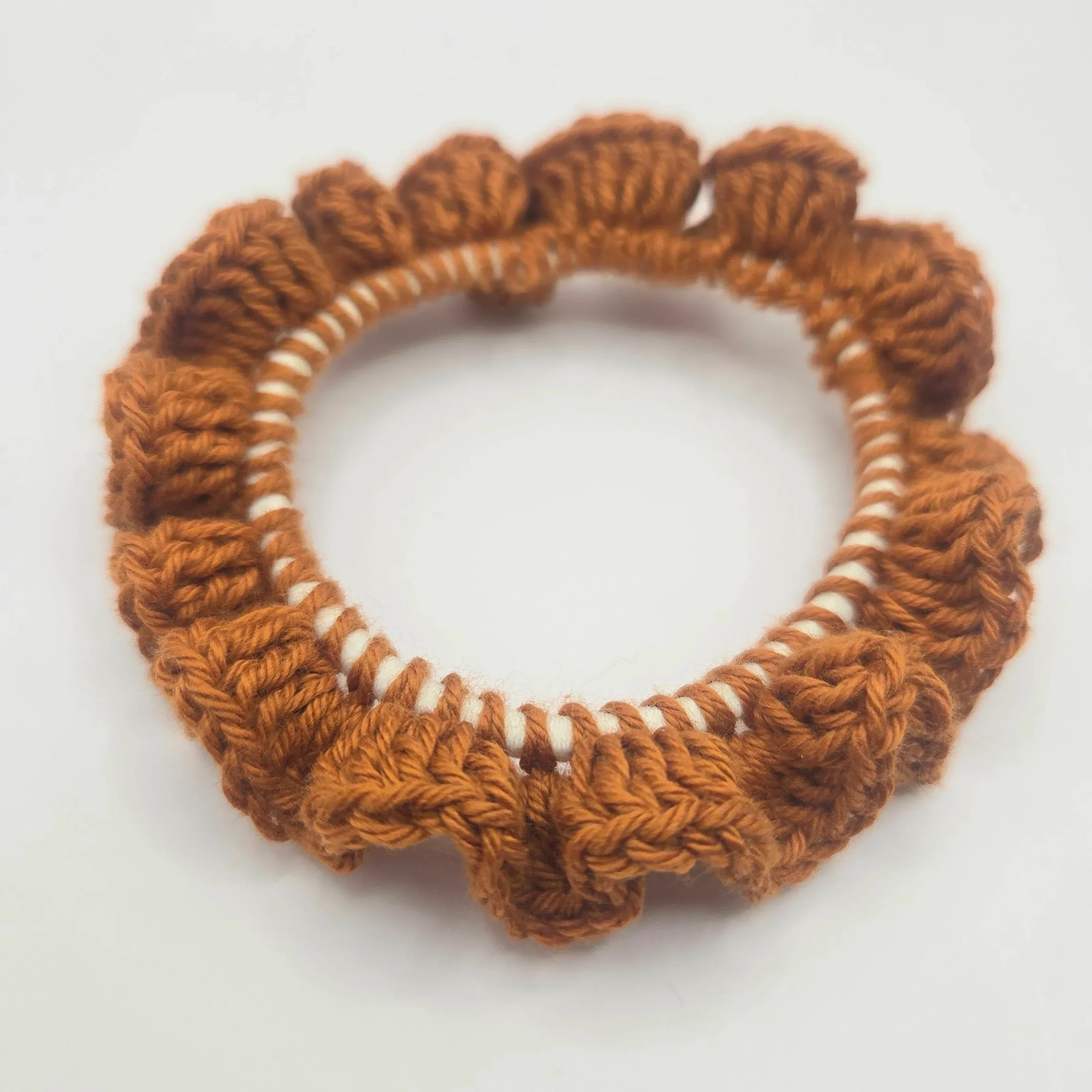 Handmade crochet scrunchie in warm brown yarn on white background
