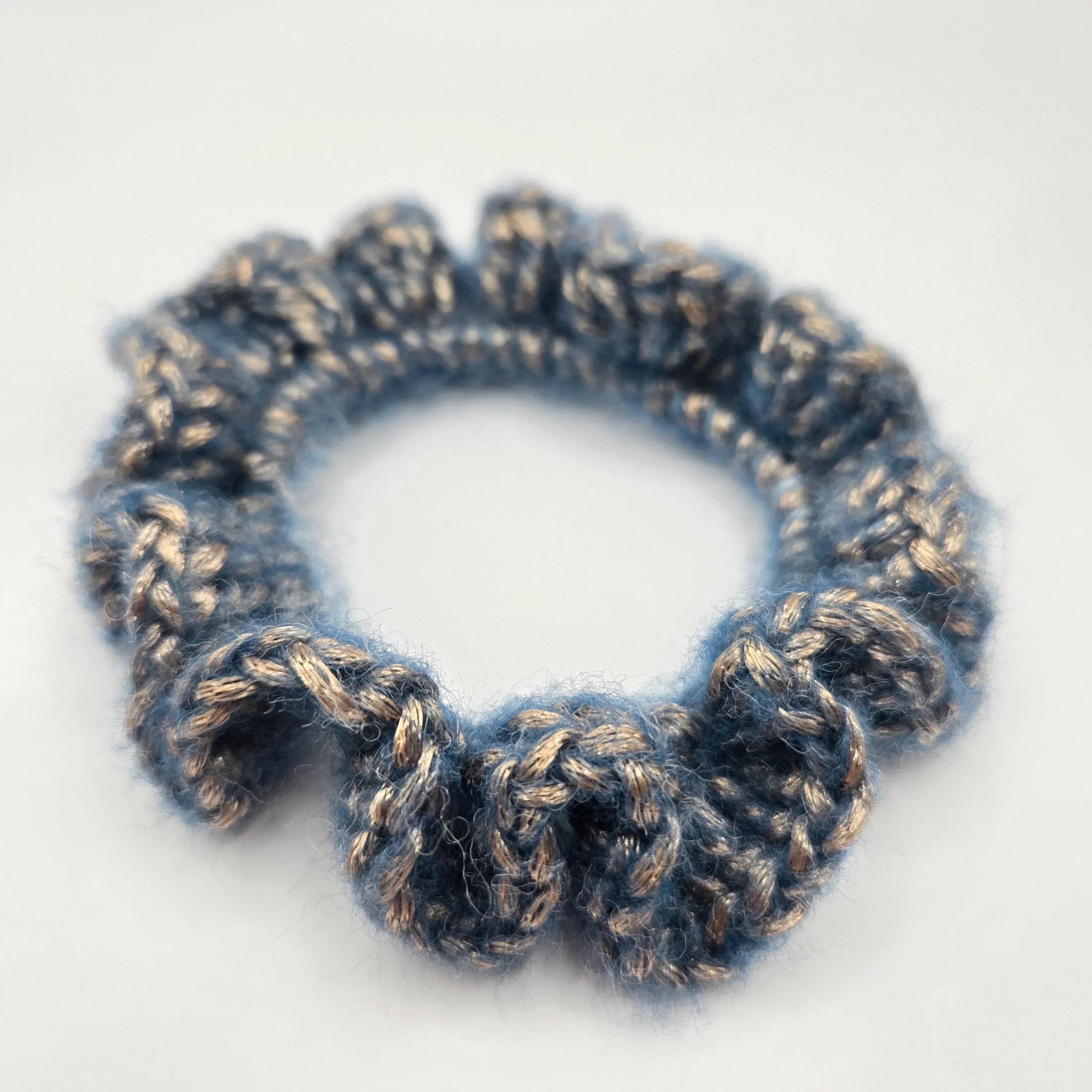 Handmade blue crochet scrunchie with gold accents on white background