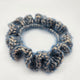 Handmade blue crochet scrunchie with gold accents on white background
