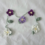 Handmade crochet flower garland with purple, lavender, and white blooms on green stems for cozy home decor