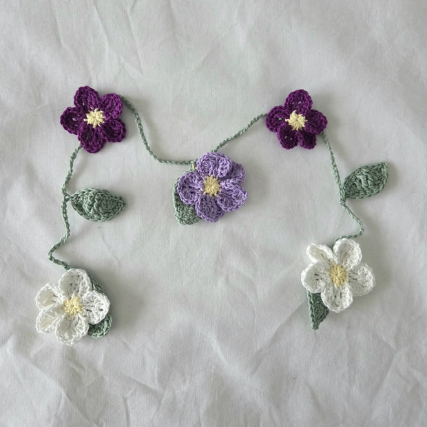 Handmade crochet floral garland with purple and white flowers on a light fabric background