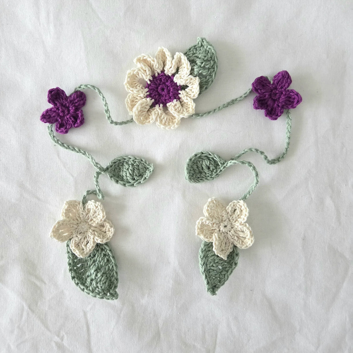 Handmade crochet flower appliqués in cream, purple, and green on white fabric background
