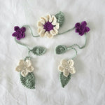 Handmade crochet flower garland with purple and cream blooms, green leaves, perfect for cozy home decor.