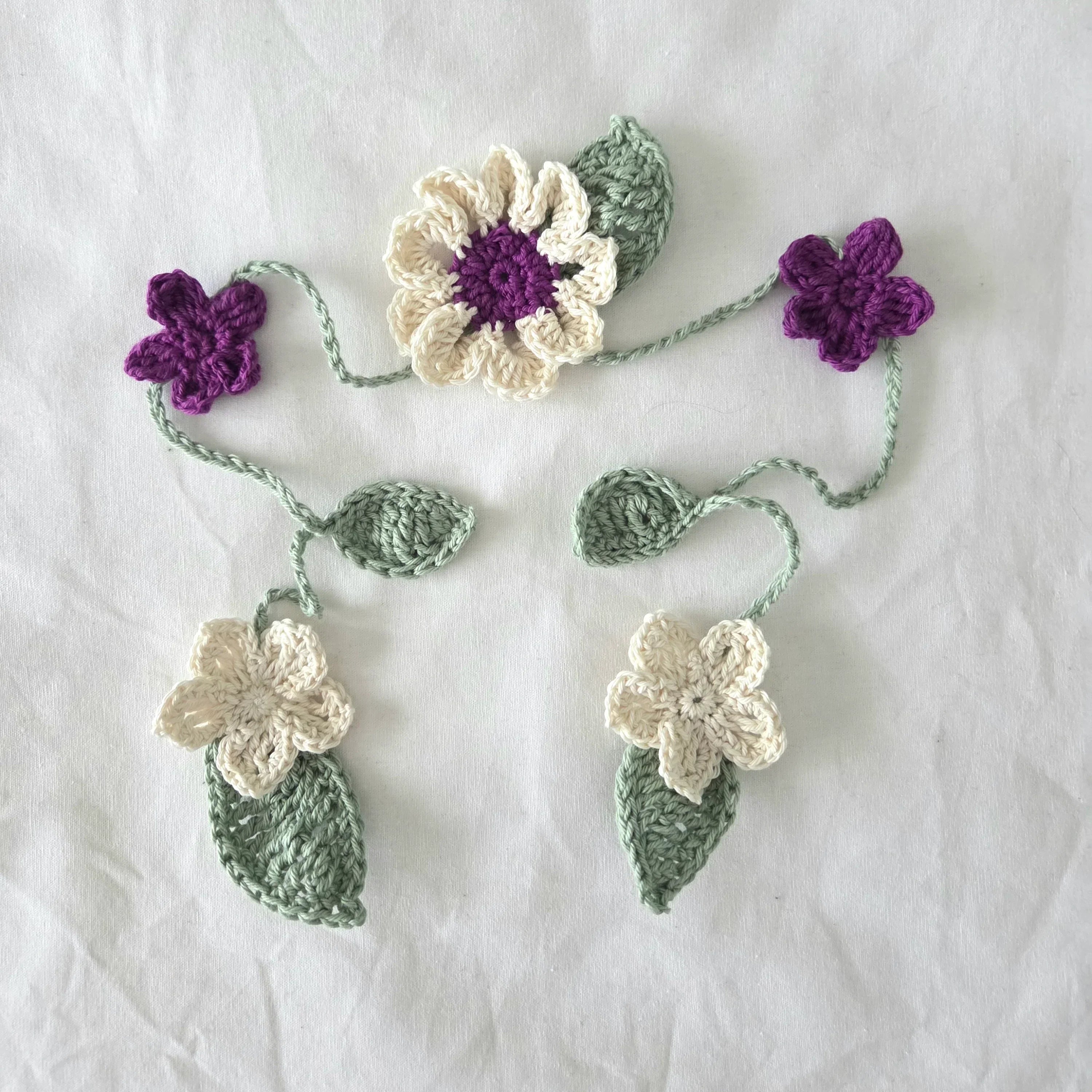 Handmade crochet flower appliqués in cream, purple, and green on white fabric background